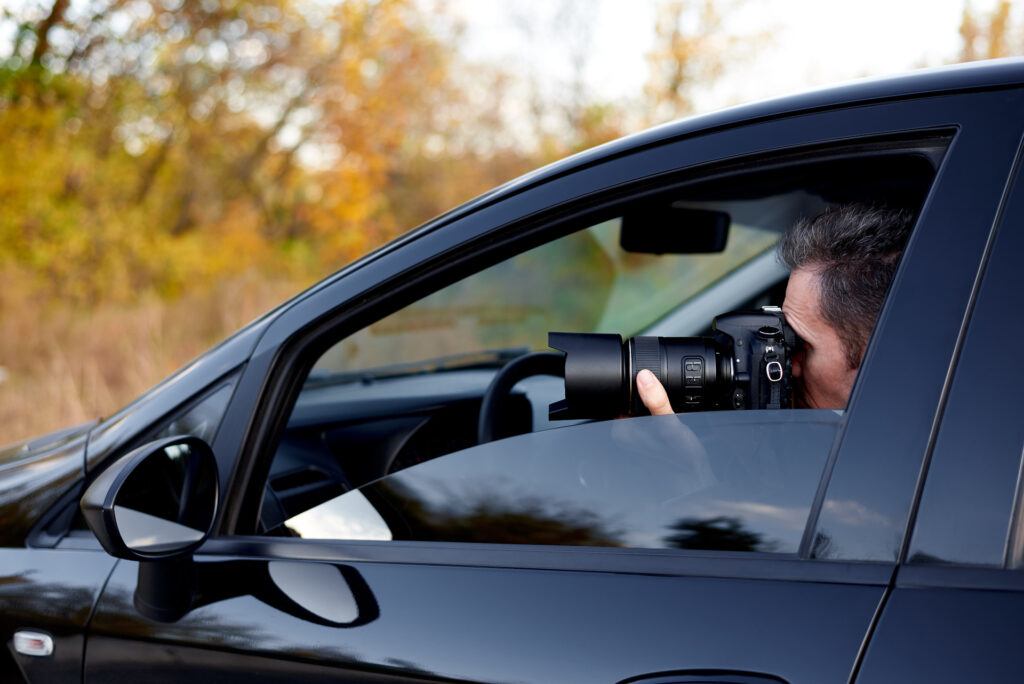 Prywatny detektyw robi zdjęcia z samochodu